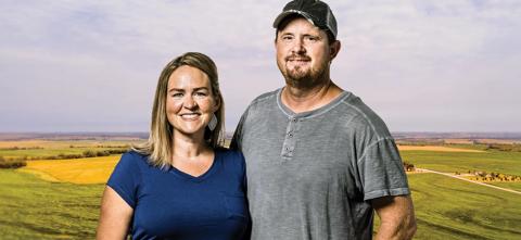 husband and wife posing in front of pasture and fields 