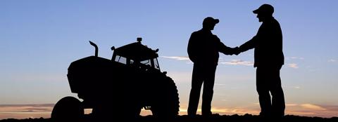 silhouette of two men shaking hands in a field with a tractor in the background