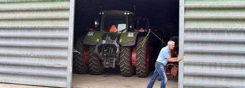 Man opening sliding shed doors revealing a tractor