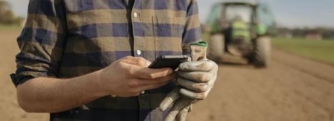 man in field looking at his mobile phone with a tractor in the background
