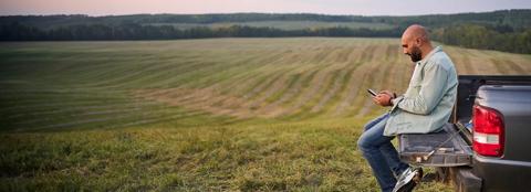 man sitting on the bed of his truck on his phone with landscape in the background