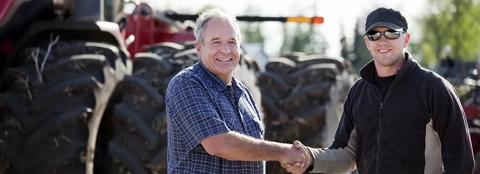 father and son shaking hands next to farm equipment