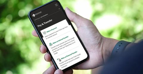 A person holding a smartphone displaying the My Account app. The background is blurred greenery. 