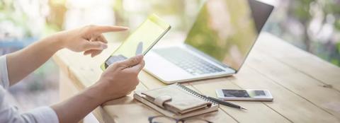 Woman's hands working at a desk on tablet and computer