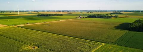 Aerial image of green farmland with wind turbines in the distance. 