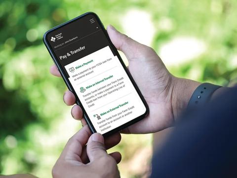 A person holding a smartphone displaying the My Account app. The background is blurred greenery. 