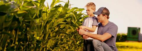 farmer and young son next to rows of corn