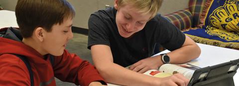 2 kids reading a textbook and iPad