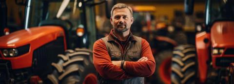 A man in  a red long sleeve shirt posing in front of red tractors