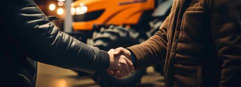 Two men shaking hands in front of a red tractor