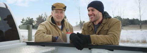 Two men smiling by the bed of a truck during winter with snow on the ground