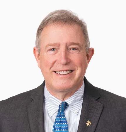 A portrait of a man wearing a dark gray suit, white striped shirt, and blue patterned tie