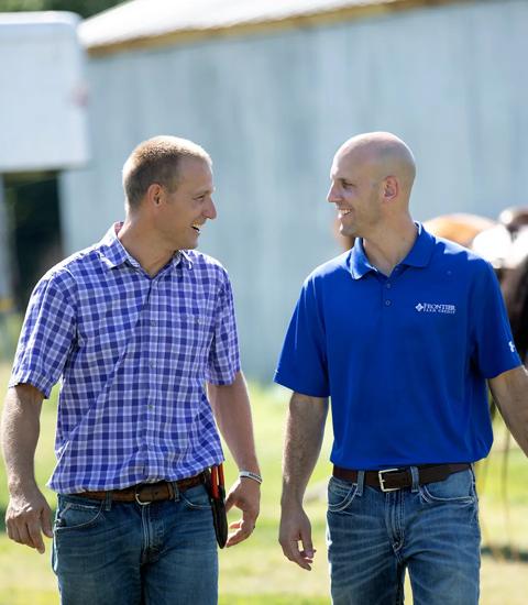 two men talking and smiling while walking on a farm 