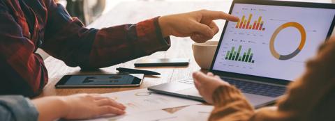 three people collaborating around a laptop with graphs on the screen