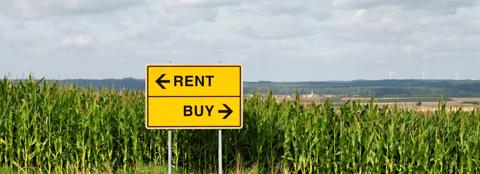 Corn field in the background with a sign in front with Rent arrow pointing left and buy arrow pointing right