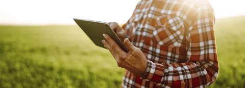 man in a red flannel shirt on a tablet in a field