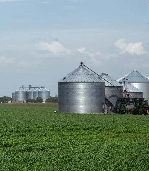 green field with multiple grain bins and farm equipment