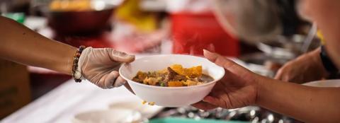 person with gloved hard passing a bowl of food to someone else